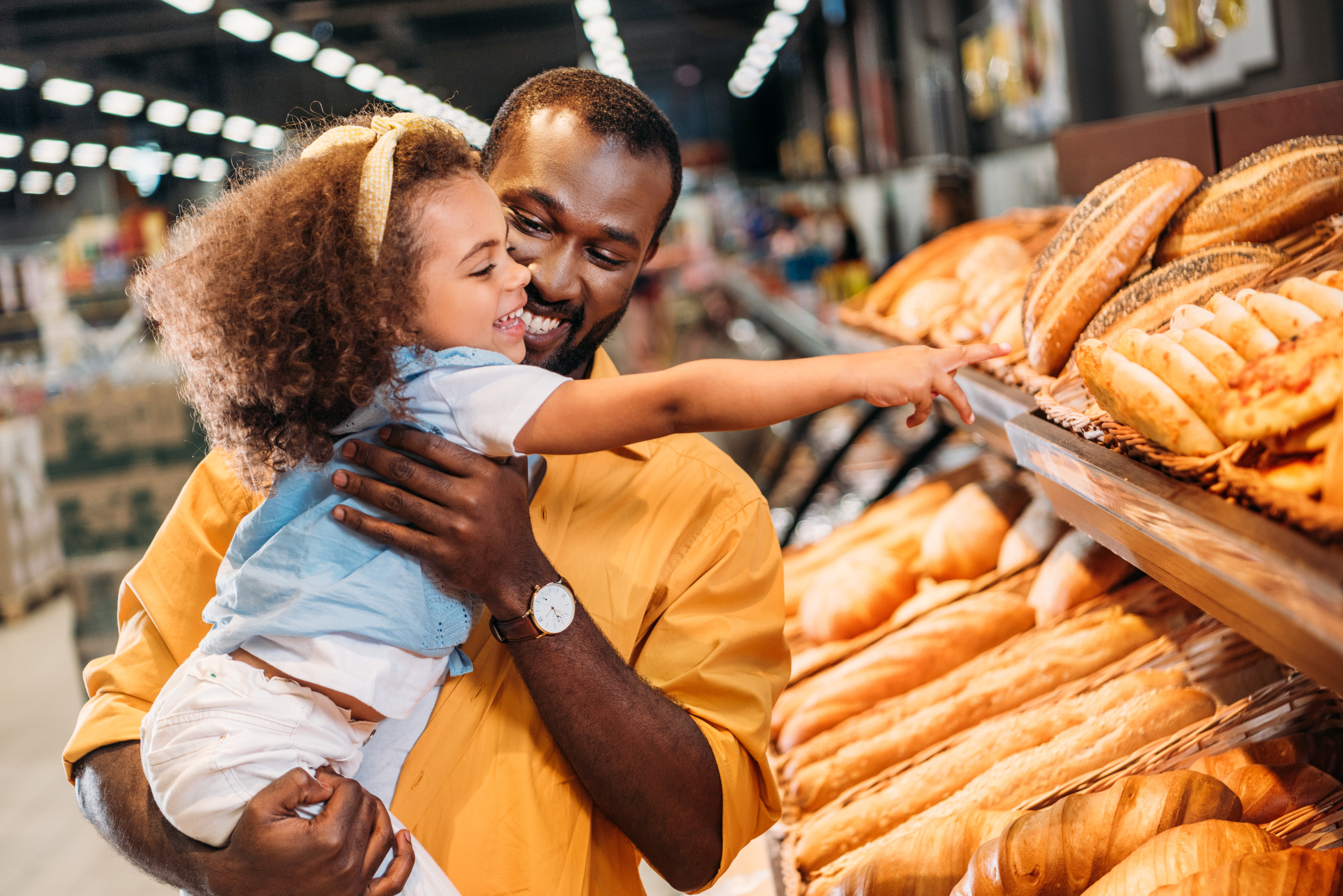 Little girl pointing at wheat bread while being held by her dad