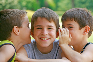 Photo of two boys whispering in another boy's ear