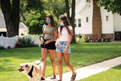 Sisters wearing masks as they walk their dog on a leash