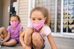 Two sisters wearing masks while drawing with chalk on their front porch