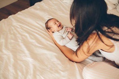 Mom laying her baby down on the bed.