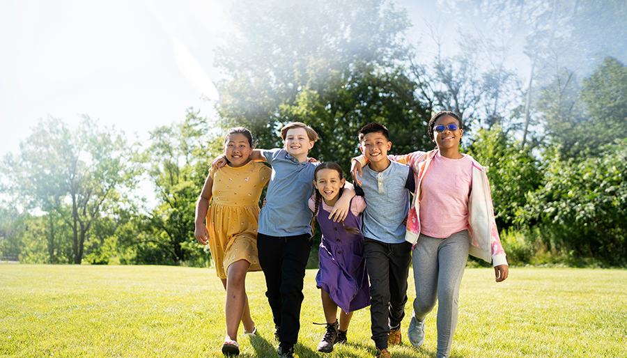 Children walking through a grassy field with the sun behind them.