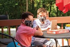 Two boys wearing masks playing on their electronic devices