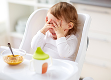 Kid eating food in highchair and covering eyes